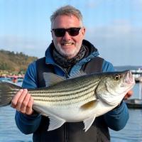 Smiling angler holding a large bass caught in Plymouth waters.